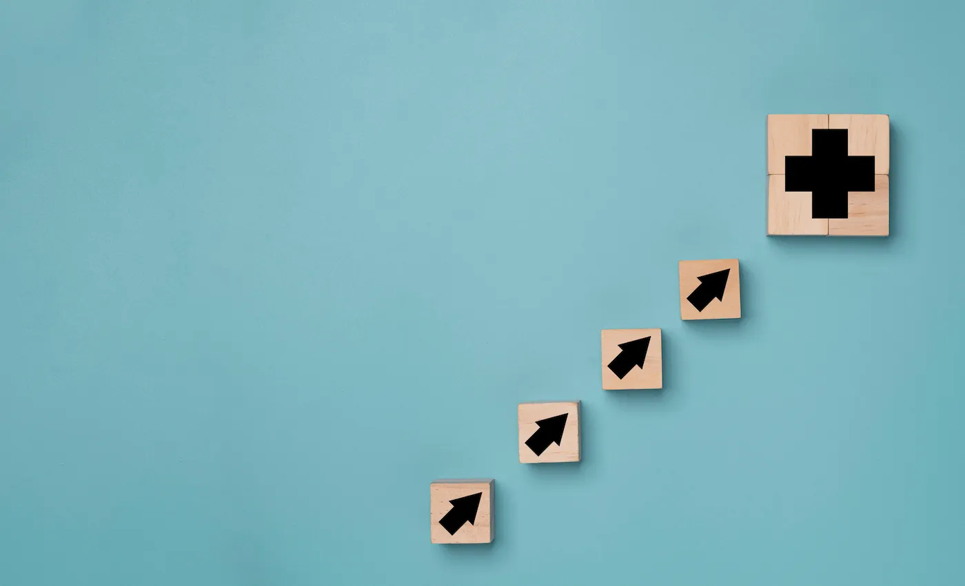 Plus sign and increasing arrow print screen on wooden cube block on blue background which it mean positive sign such as more benefit thinking and mindset concept. (Plus sign and increasing arrow print screen on wooden cube block on blue background whi