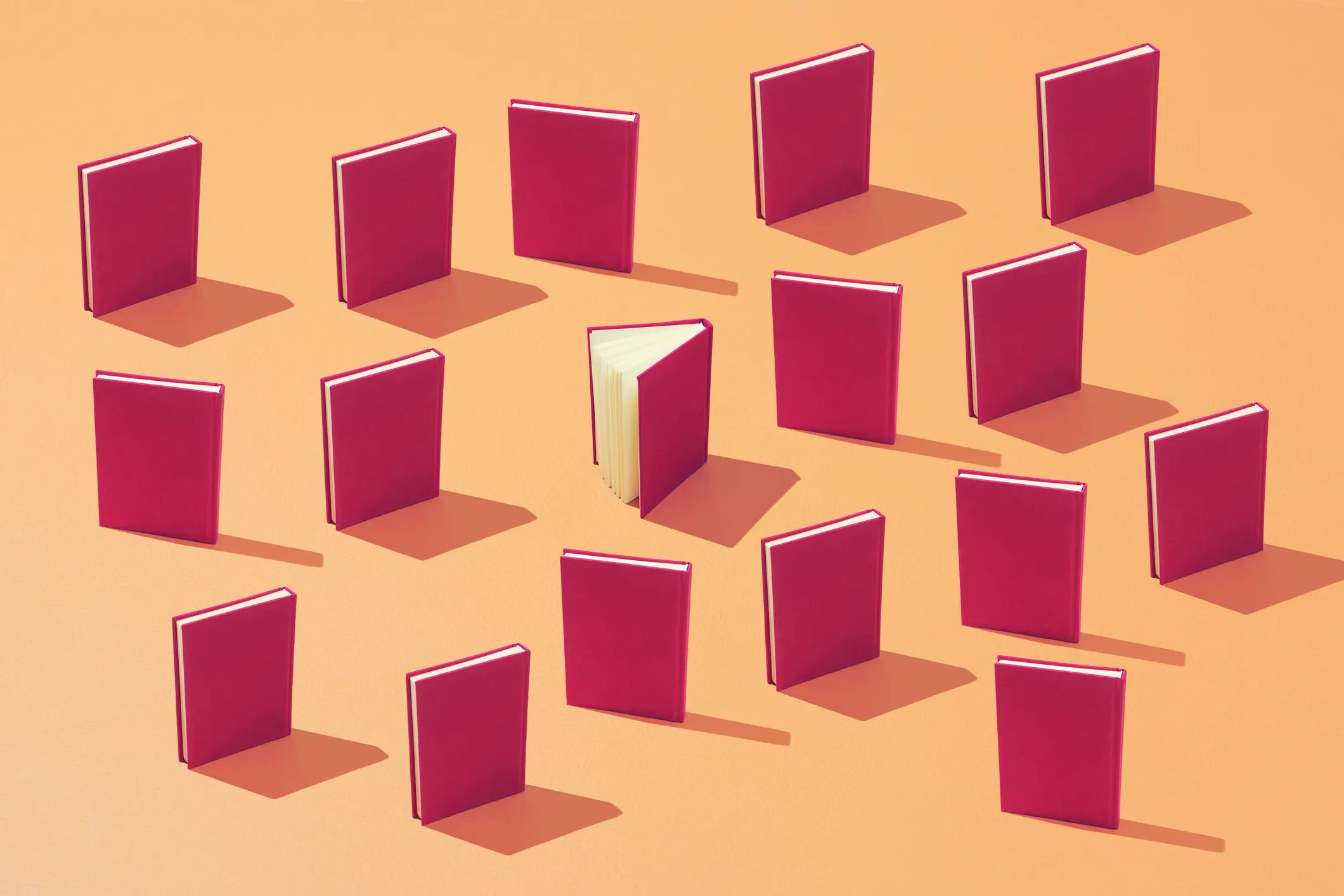 A group of books laid in a pattern on a colorful background. one is standing out from the crowd
