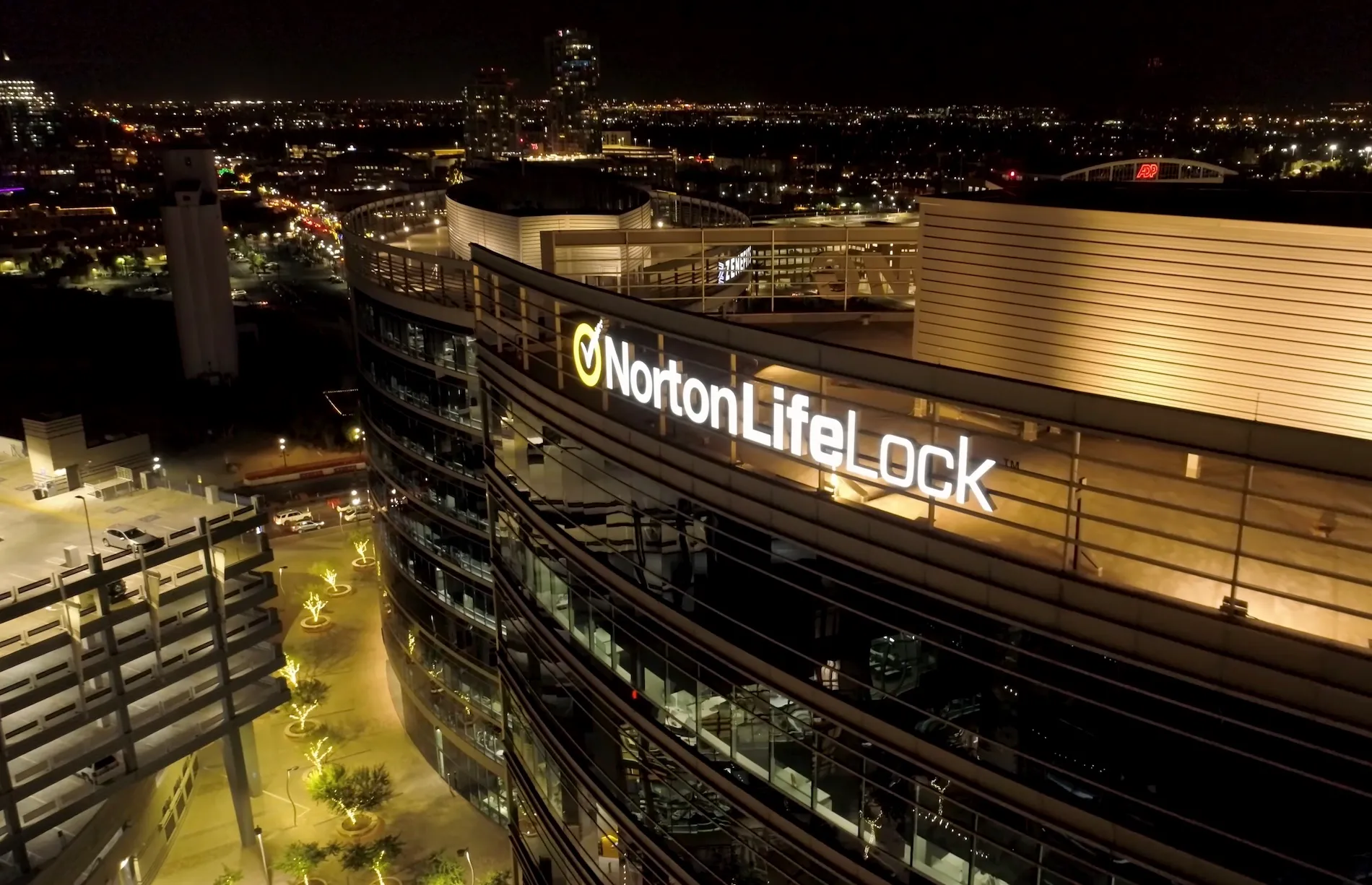 a snapshot of a flyover of the top of Norton Lifelock's offices at night with a city silhouette in the background