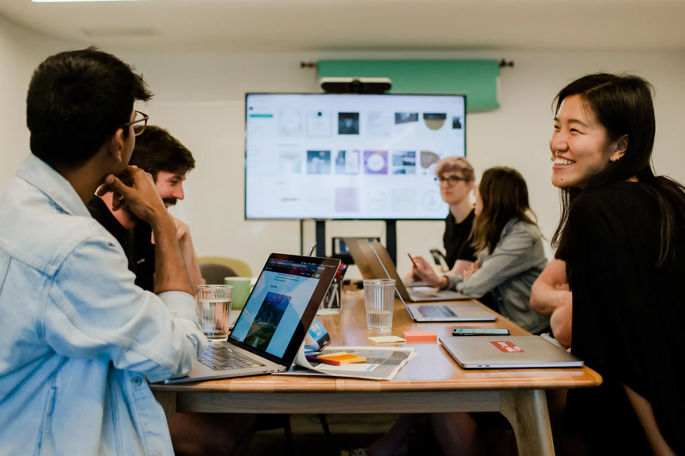 Students sitting around a table, laptops open, large monitor at one end