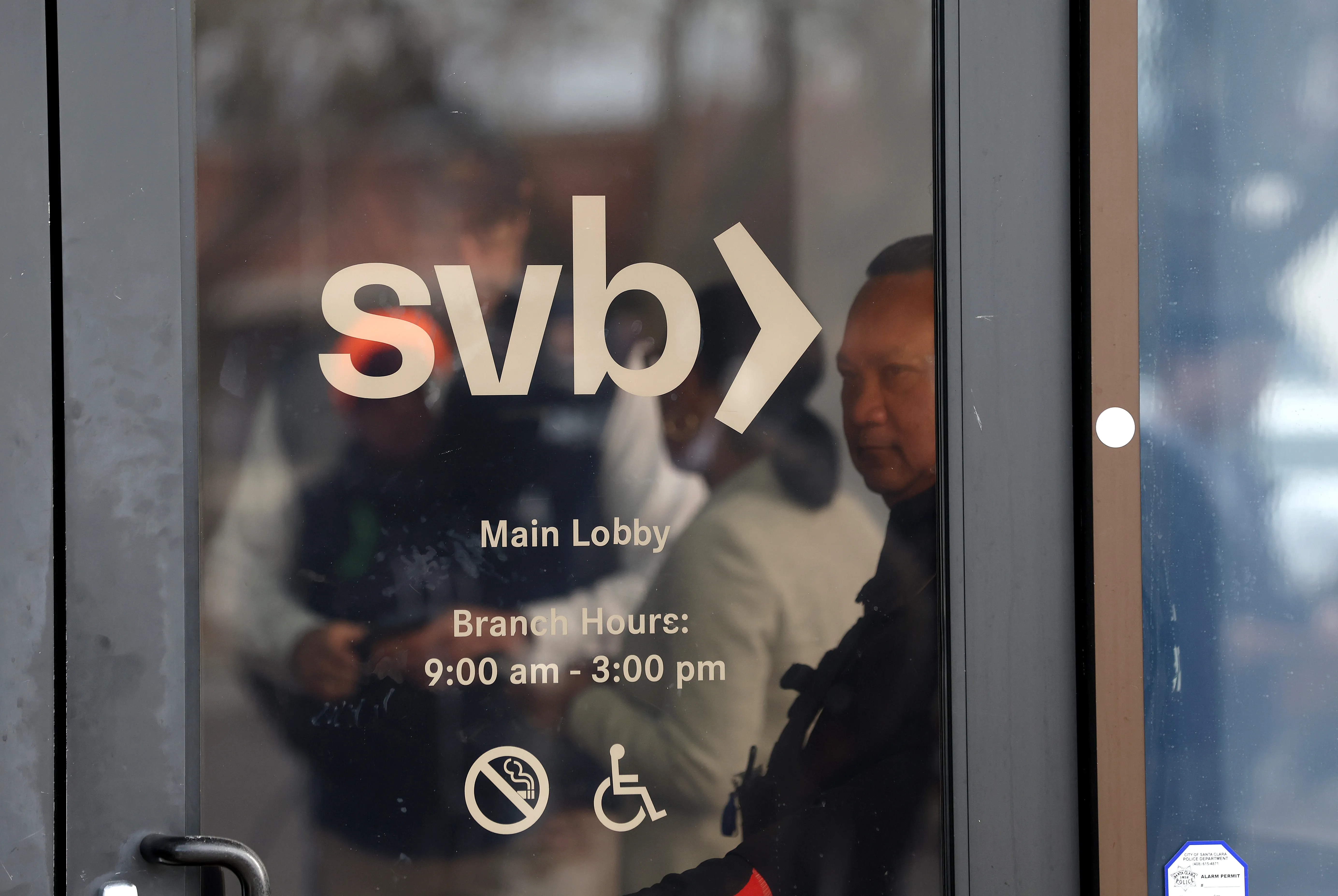 A security guard at Silicon Valley Bank monitors a line of people outside the office on March 13, 2023 in Santa Clara, California
