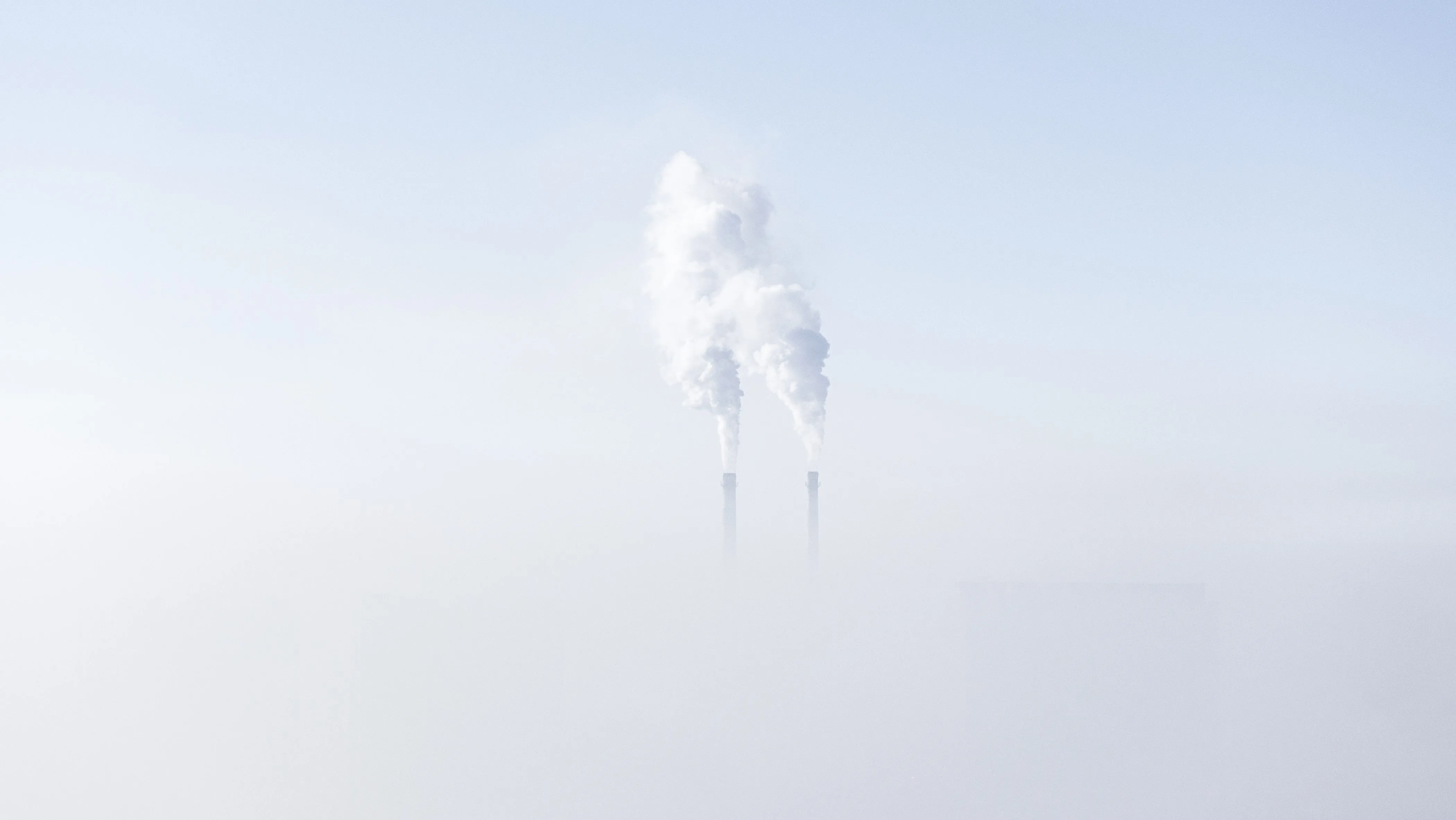 Smoke stacks emit pollution above a layer of fog.