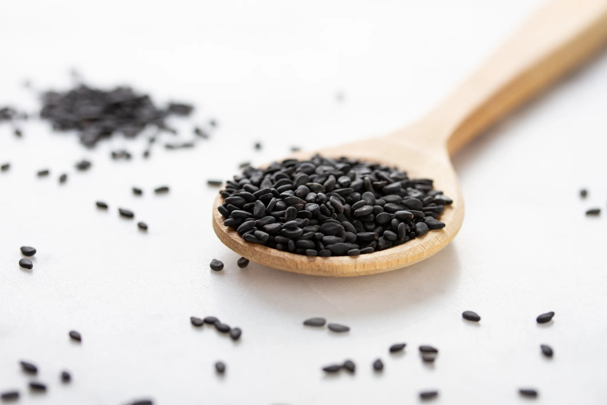 Black sesame seeds in a wooden spoon on a white background