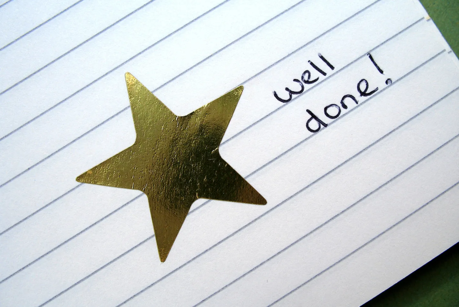 A gold star on a piece of lined paper next to a handwritten note that reads, "well done!"
