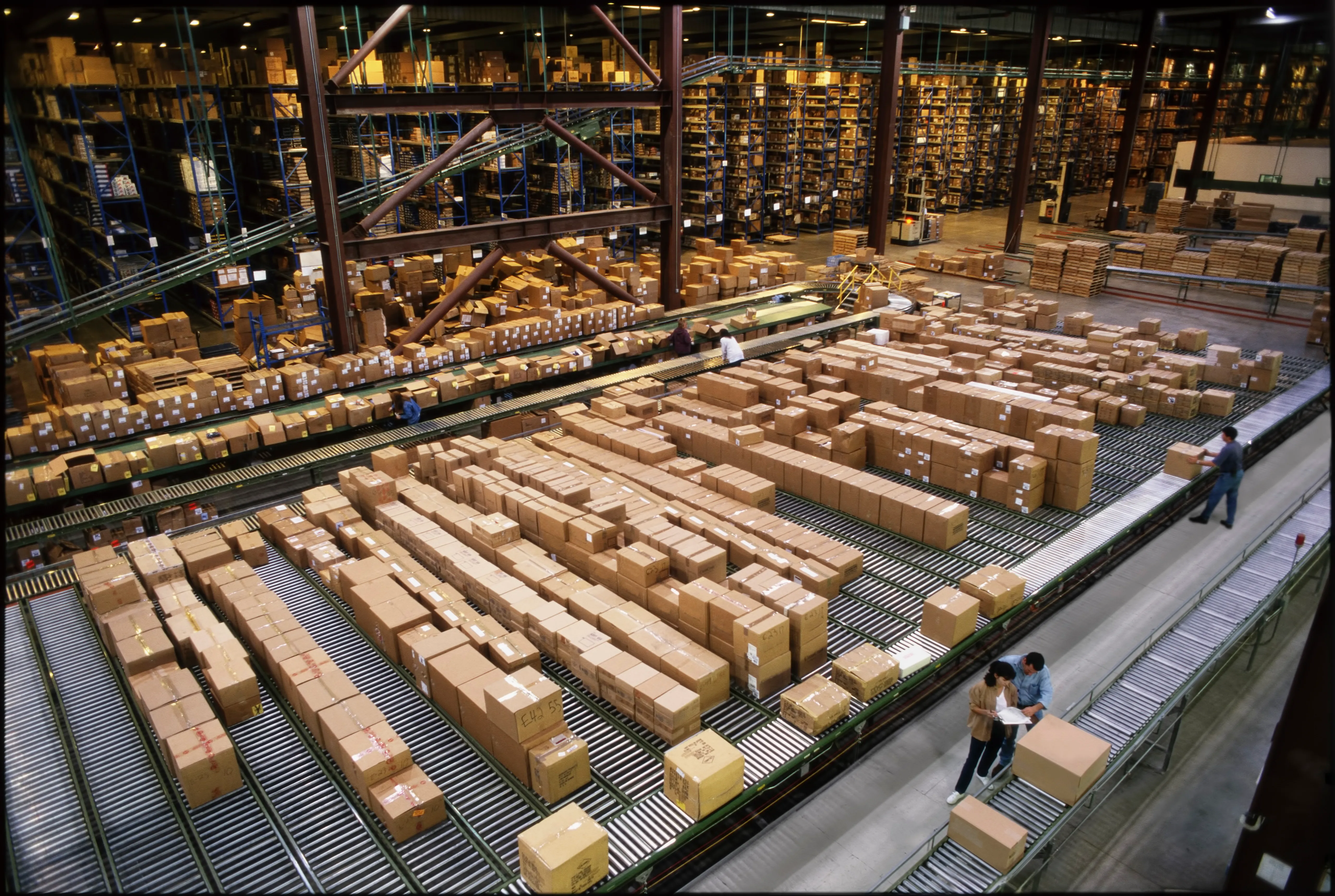 Overview of a large industrial distribution warehouse storing products in cardboard boxes on conveyor belts and racks.
