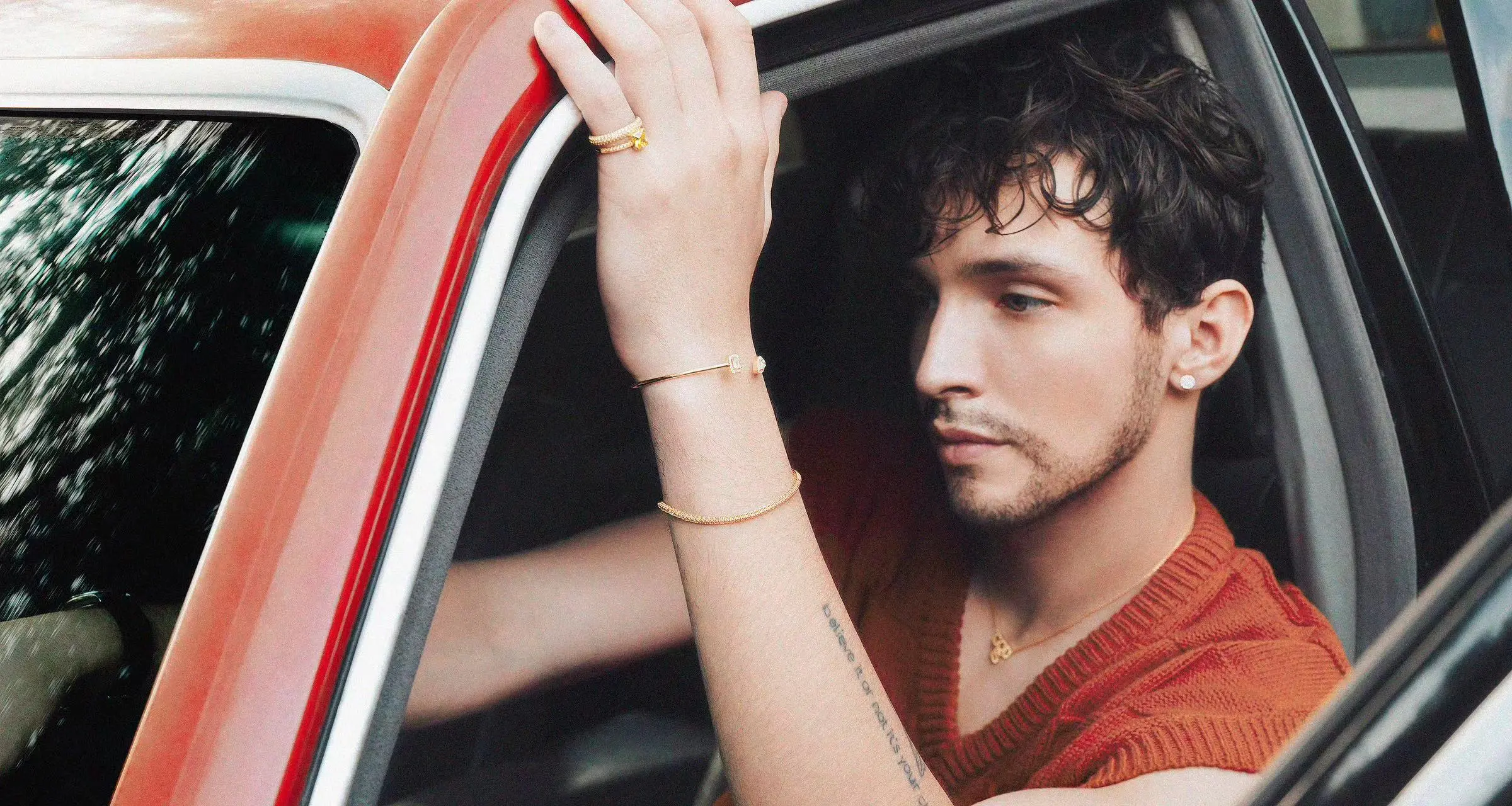 man sitting in car, jewelry on arm in open window