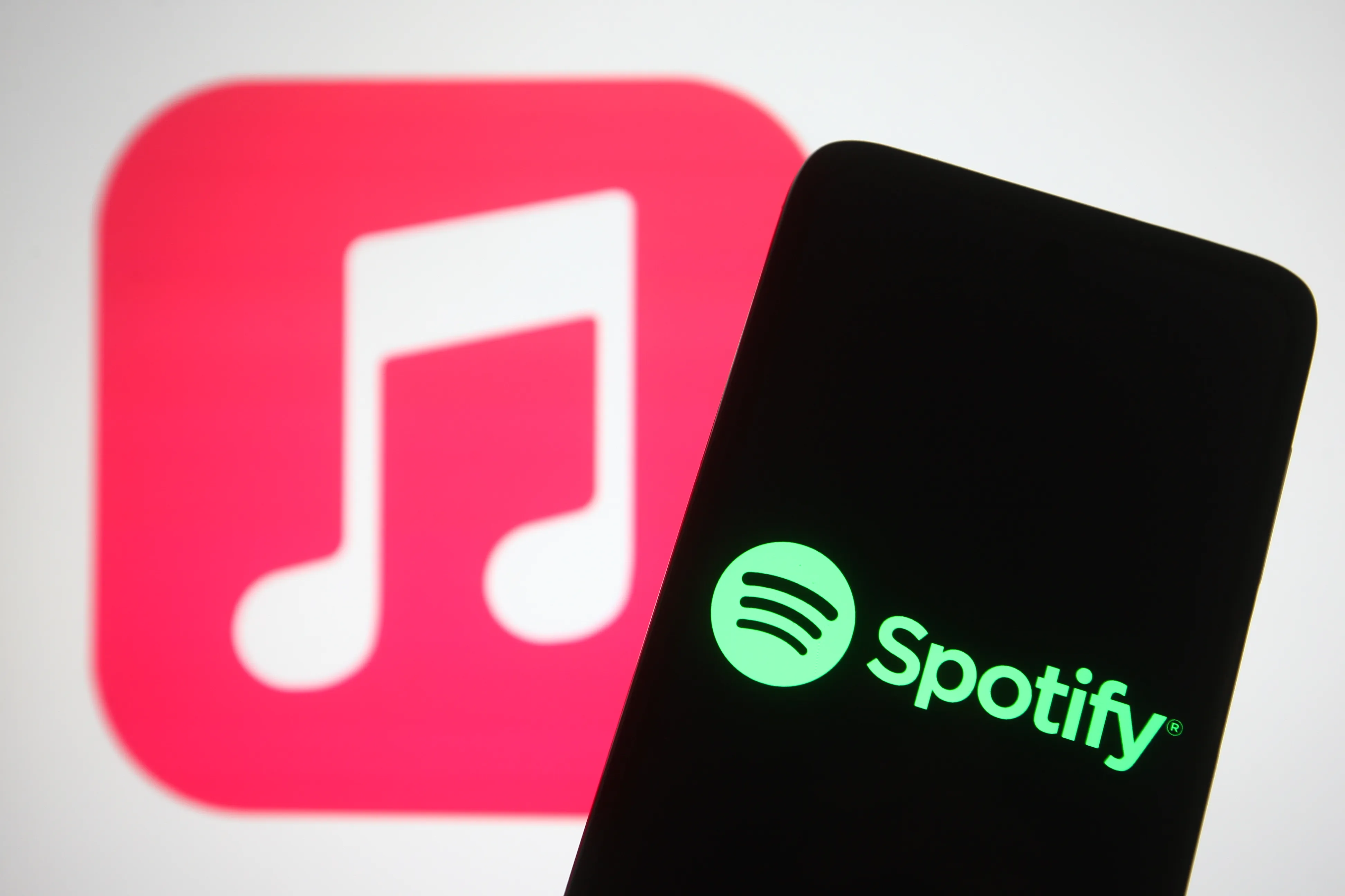 The Spotify logo seen displayed on a smartphone screen in front of Apple Music logo in the background.