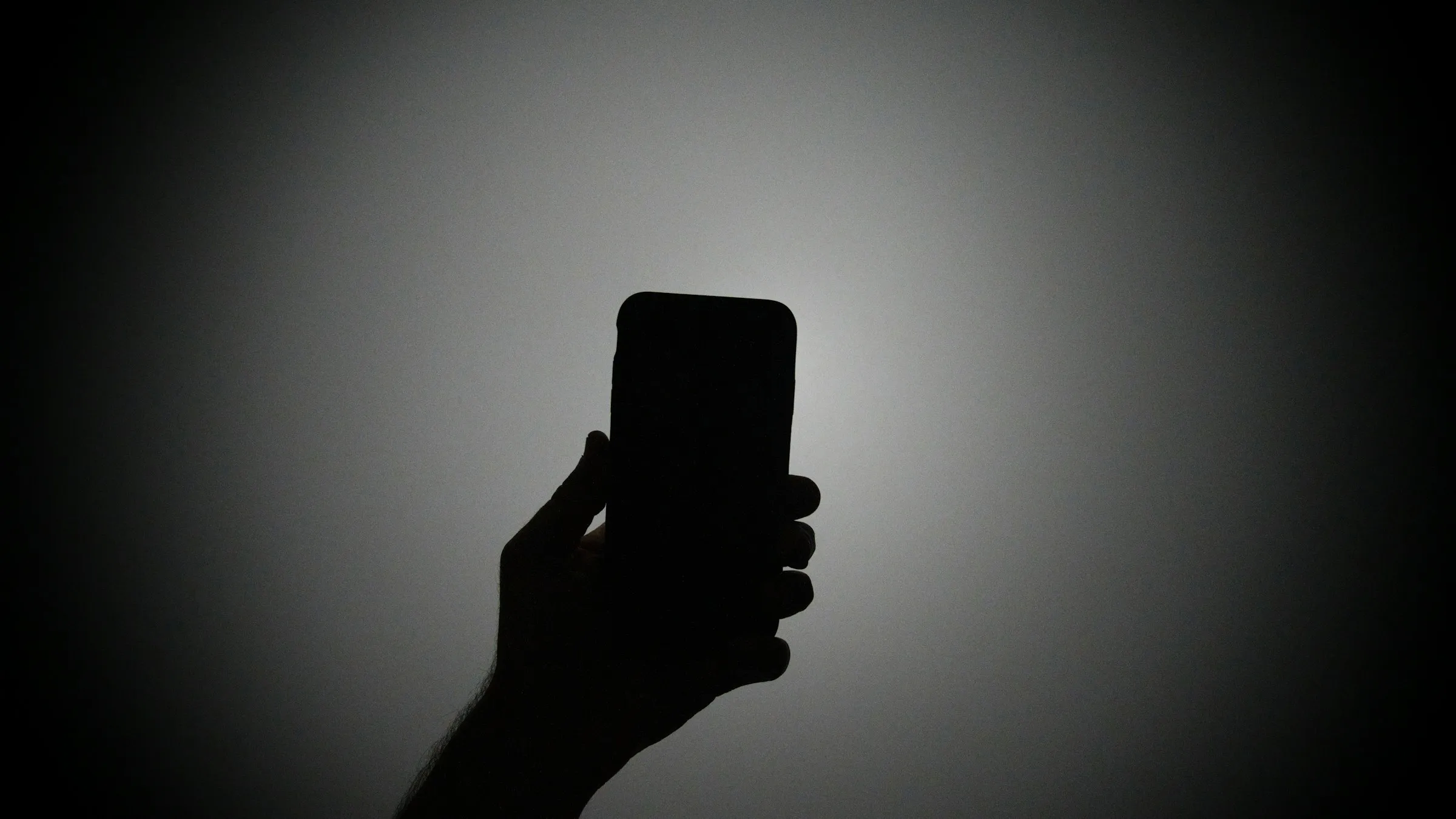 The silhouette of a hand holding an iPhone with the light on.